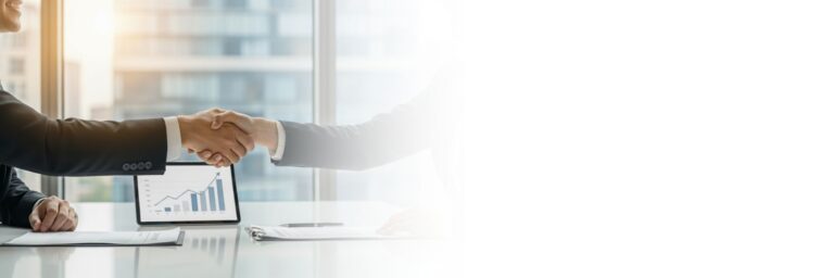 Zwei Geschäftspartner geben sich über einem Tisch die Hand, auf dem ein elektronisches Tablet mit Finanzdaten liegt.